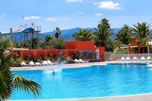 Una piscina con agua azul cristalina, rodeada de palmeras y un edificio rojo.