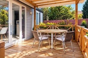 A wooden deck with a table and chairs, a sliding glass door, and a view of greenery.