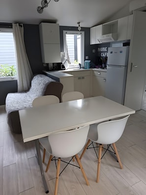 A compact kitchen with a dining area, a sofa, and a window with curtains. - Mobile Home 'Mobil-home Piscine, Clim Et Wifi' with Shared Pool, Wi-Fi and Air Conditioning (Argelès-sur-Mer)