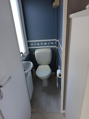 A compact bathroom with a toilet, sink, and a window. - Mobile Home 'Mobil-home Piscine, Clim Et Wifi' with Shared Pool, Wi-Fi and Air Conditioning (Argelès-sur-Mer)