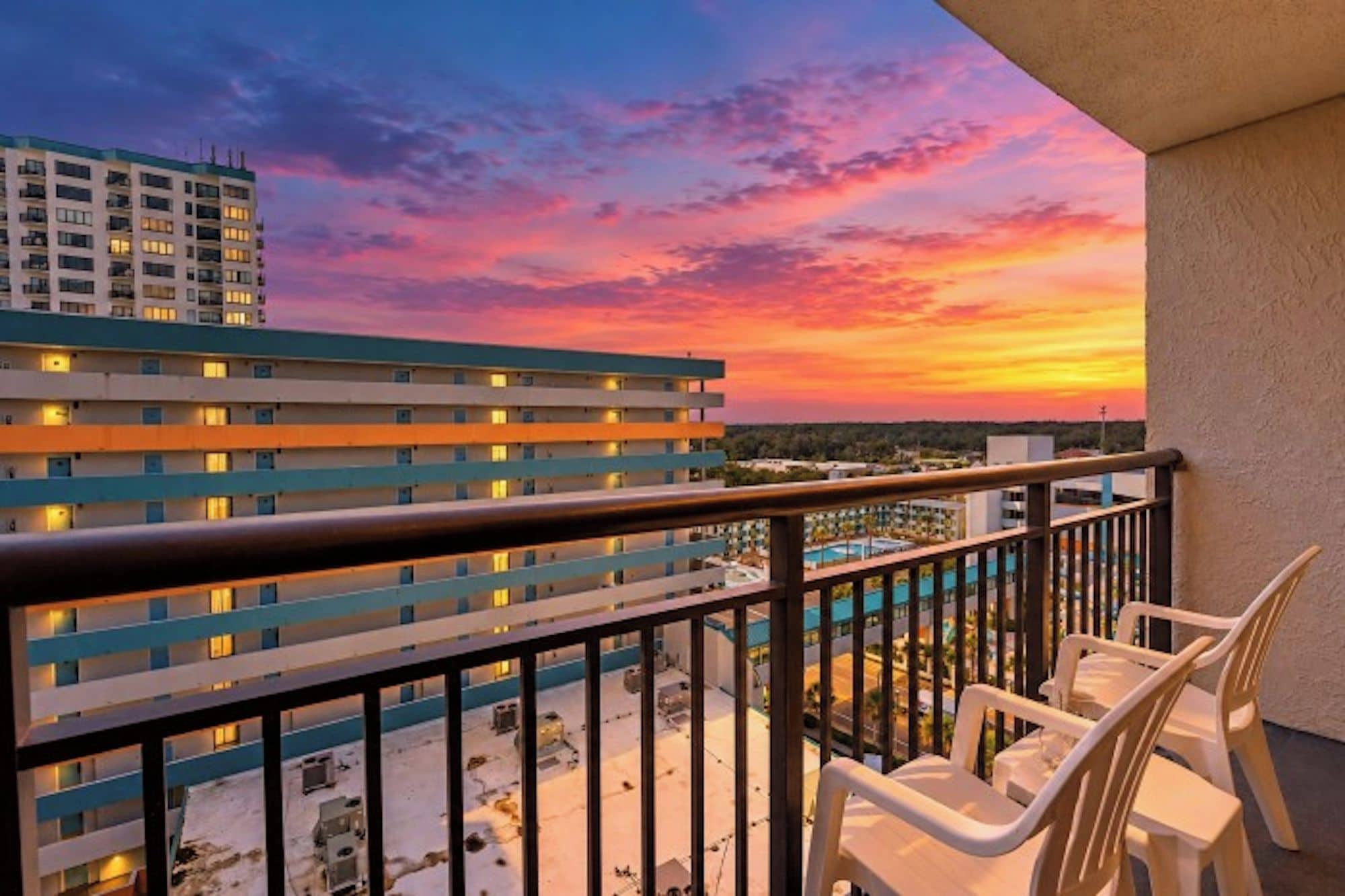 A balcony with a view of a hotel building and a pool area during sunset.