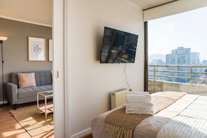 Ein modernes Schlafzimmer mit Bett, Sofa, Fernseher und Blick auf eine Stadtlandschaft.