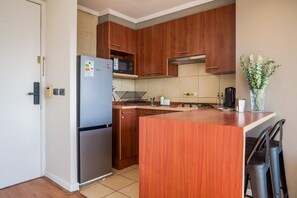 Una cucina compatta con mobili in legno, un frigorifero in acciaio inossidabile, un forno a microonde e un piccolo bancone con lavello.