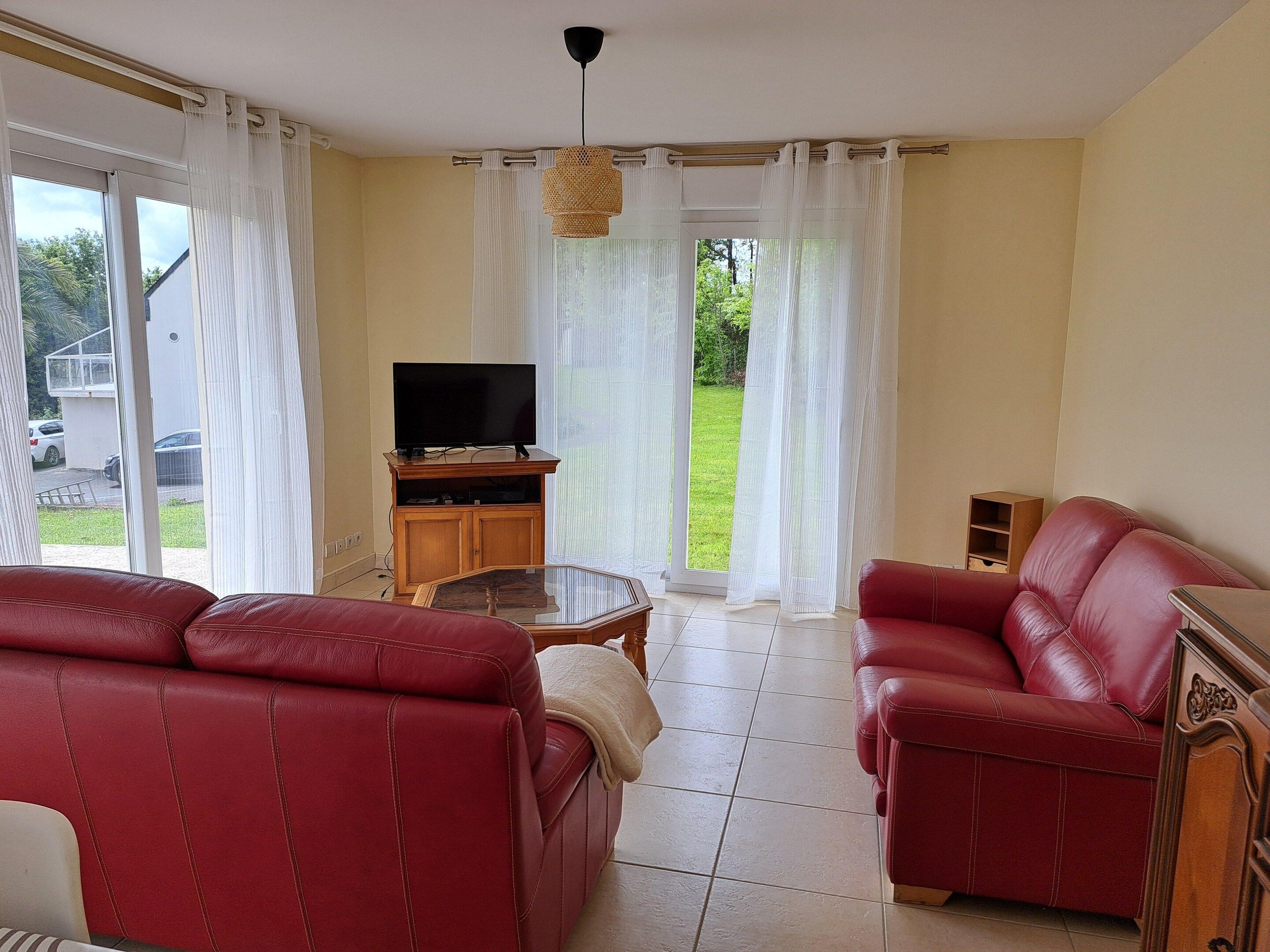 A living room with red leather sofas, a wooden entertainment unit with a TV, and a glass coffee table.