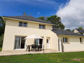 A two-story house with a patio area featuring a table and chairs, a white umbrella, and a door leading to the interior. - Sea-view Holiday Home in Hanvec for 5 (Hanvec)