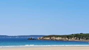 A beach with clear skies, calm water, and a rocky coastline.