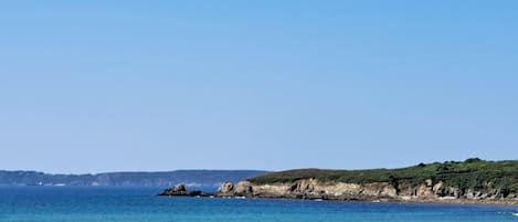 A beach with clear skies, calm water, and a rocky coastline.