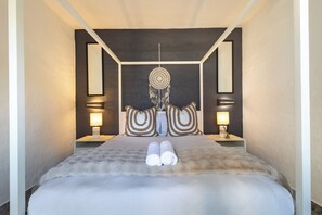 A neatly made bed with two rolled towels, a dreamcatcher, and two wall-mounted lamps. - Santorini Ballito | 180º Sea Views, Braai and Pool (Cape Town)