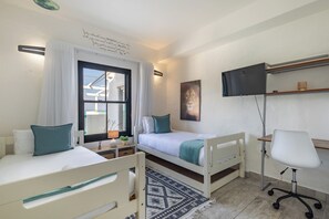 A bedroom with two single beds, a desk with a chair, a television, and a window with curtains. - Santorini Ballito | 180º Sea Views, Braai and Pool (Cape Town)