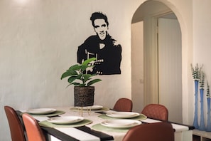 A dining area with a table set for four, a potted plant, and a wall-mounted painting. - Santorini Ballito | 180º Sea Views, Braai and Pool (Cape Town)