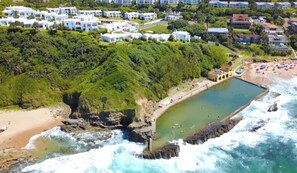 A coastal area with a rocky beach, a swimming pool, and a residential area with white buildings. - Santorini Ballito | 180º Sea Views, Braai and Pool (Cape Town)