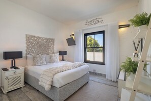 A modern bedroom with a large bed, two bedside tables, a decorative wall piece, a window with curtains, and a potted plant. - Santorini Ballito | 180º Sea Views, Braai and Pool (Cape Town)