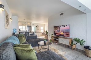 A modern living room with a grey sofa, a coffee table, and a TV on a wooden stand. - Santorini Ballito | 180º Sea Views, Braai and Pool (Cape Town)