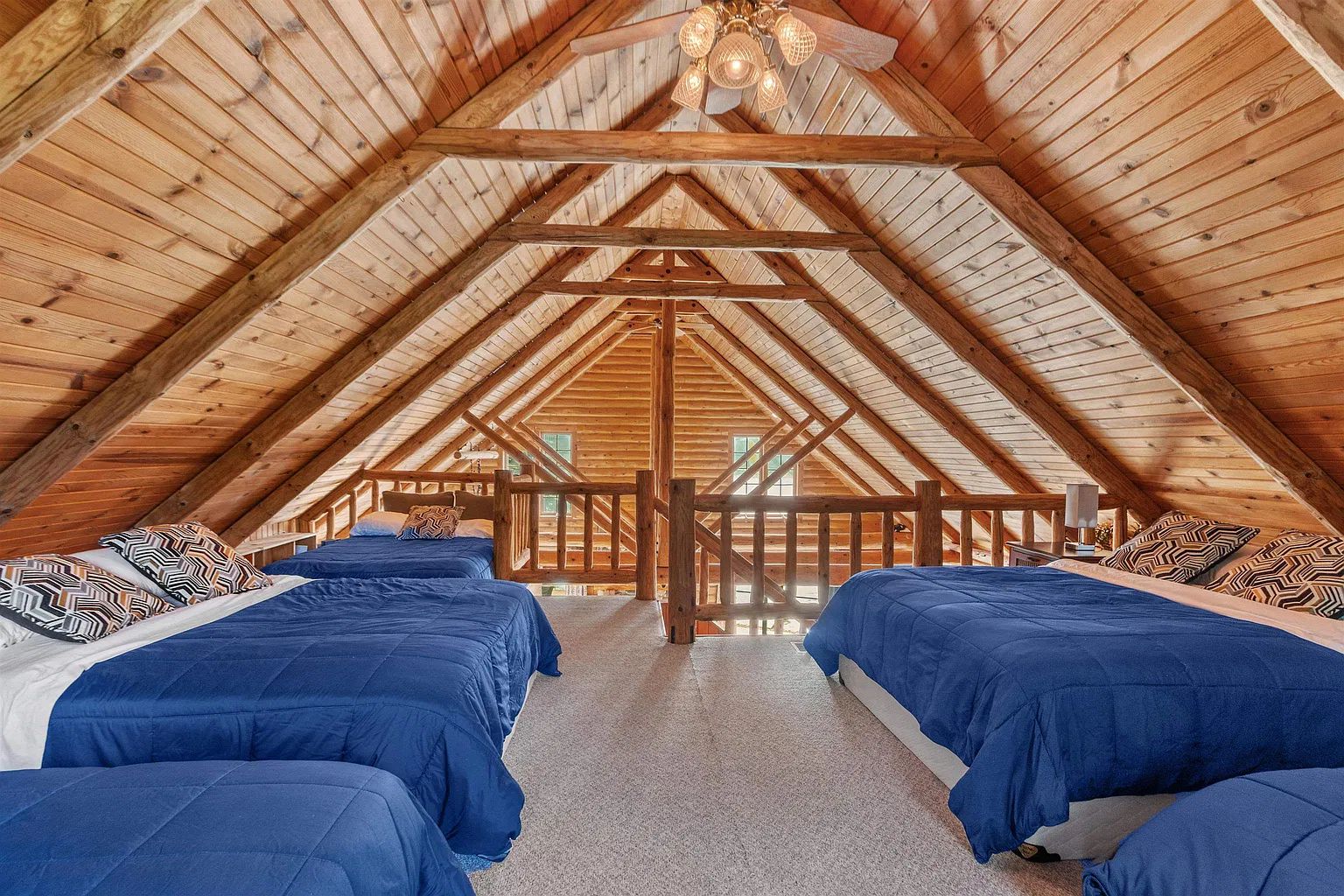 Une pièce aux hauts plafonds, dotée d’un toit en bois à pente, de deux lits avec une literie bleue et d’une rambarde centrale en bois.