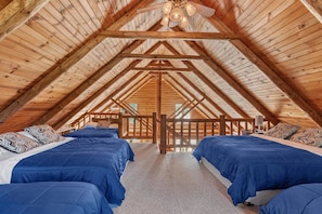Een kamer met hoge plafonds en een schuin houten dak, met twee bedden voorzien van blauw beddengoed en een houten balustrade in het midden.