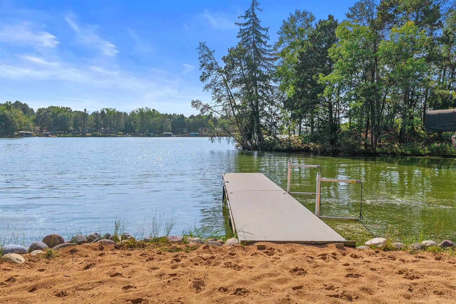 Una platja sorrenca amb un moll de fusta que s'endinsa en un llac, envoltat d'arbres.