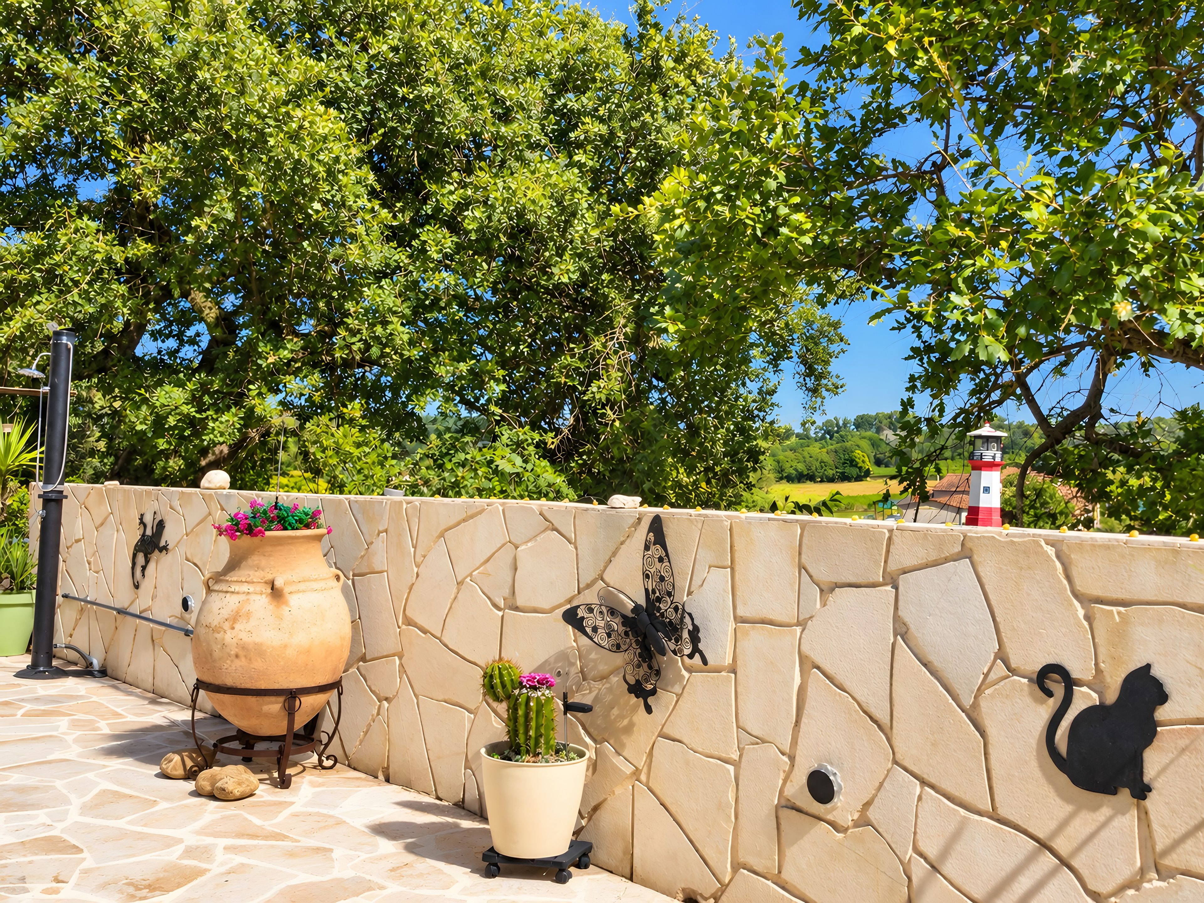 A stone wall with decorative wall art, a potted plant, and a large pot on a patio.