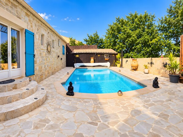 A stone pool with a statue, a wooden house, and a stone wall.