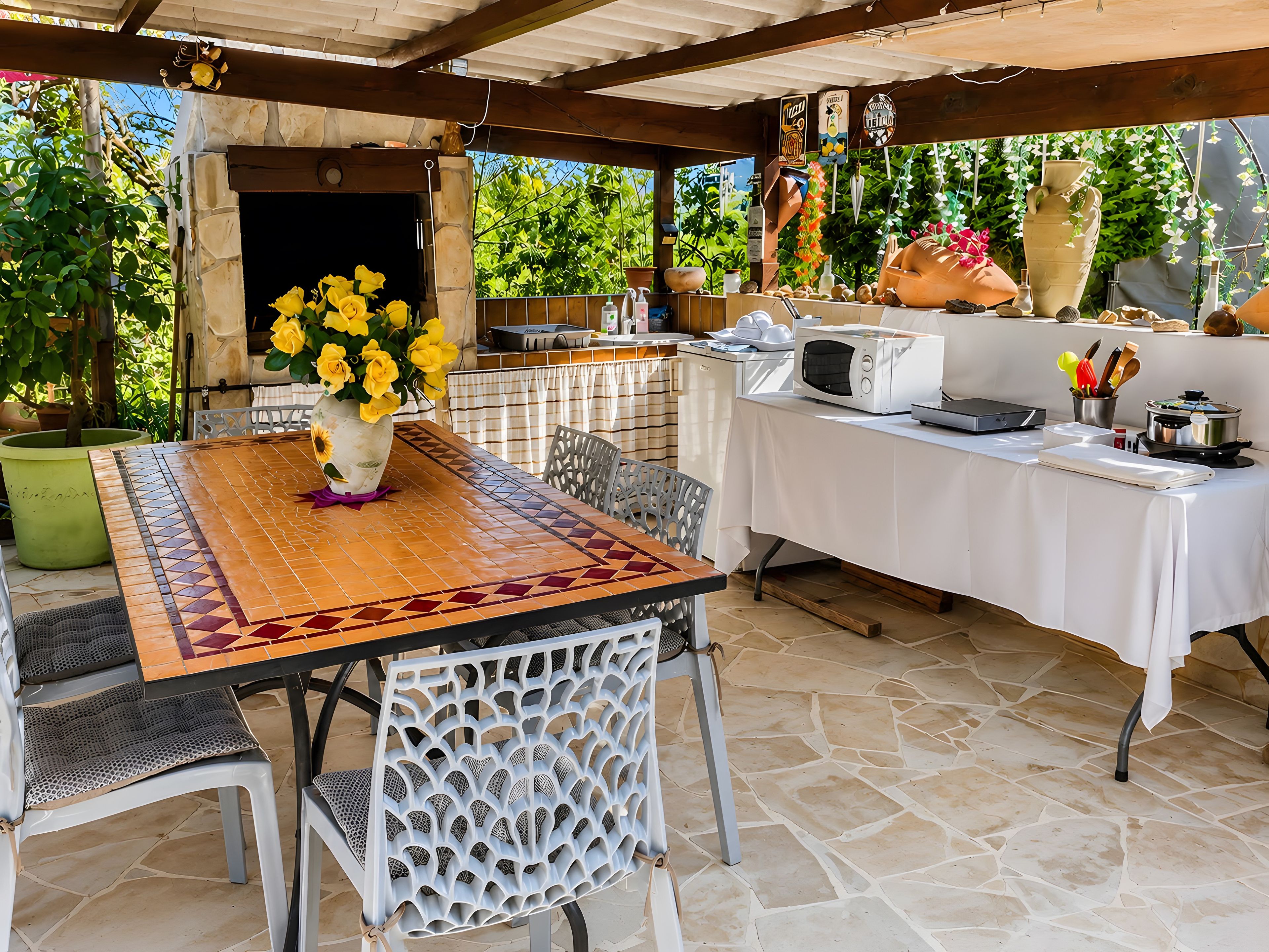Eine Terrasse im Freien mit einem gefliesten Tisch, Stühlen, einer Mikrowelle und einem Steinfußboden.