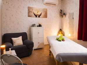 Une pièce comprenant une table de massage, un fauteuil de massage, un meuble et un climatiseur fixé au mur.