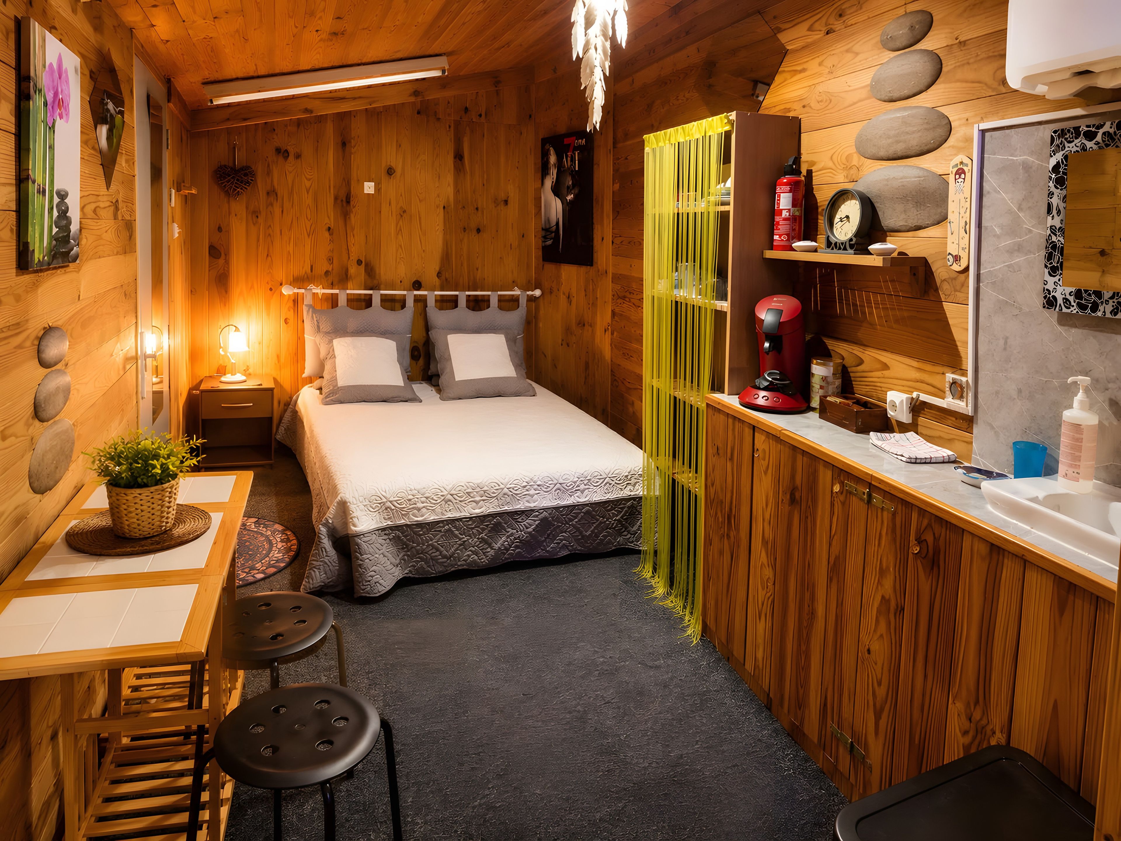 Ein gemütliches Holzhaus mit einem Bett, einem kleinen Tisch mit einer Pflanze, einer Kaffeemaschine und einem Waschbecken.