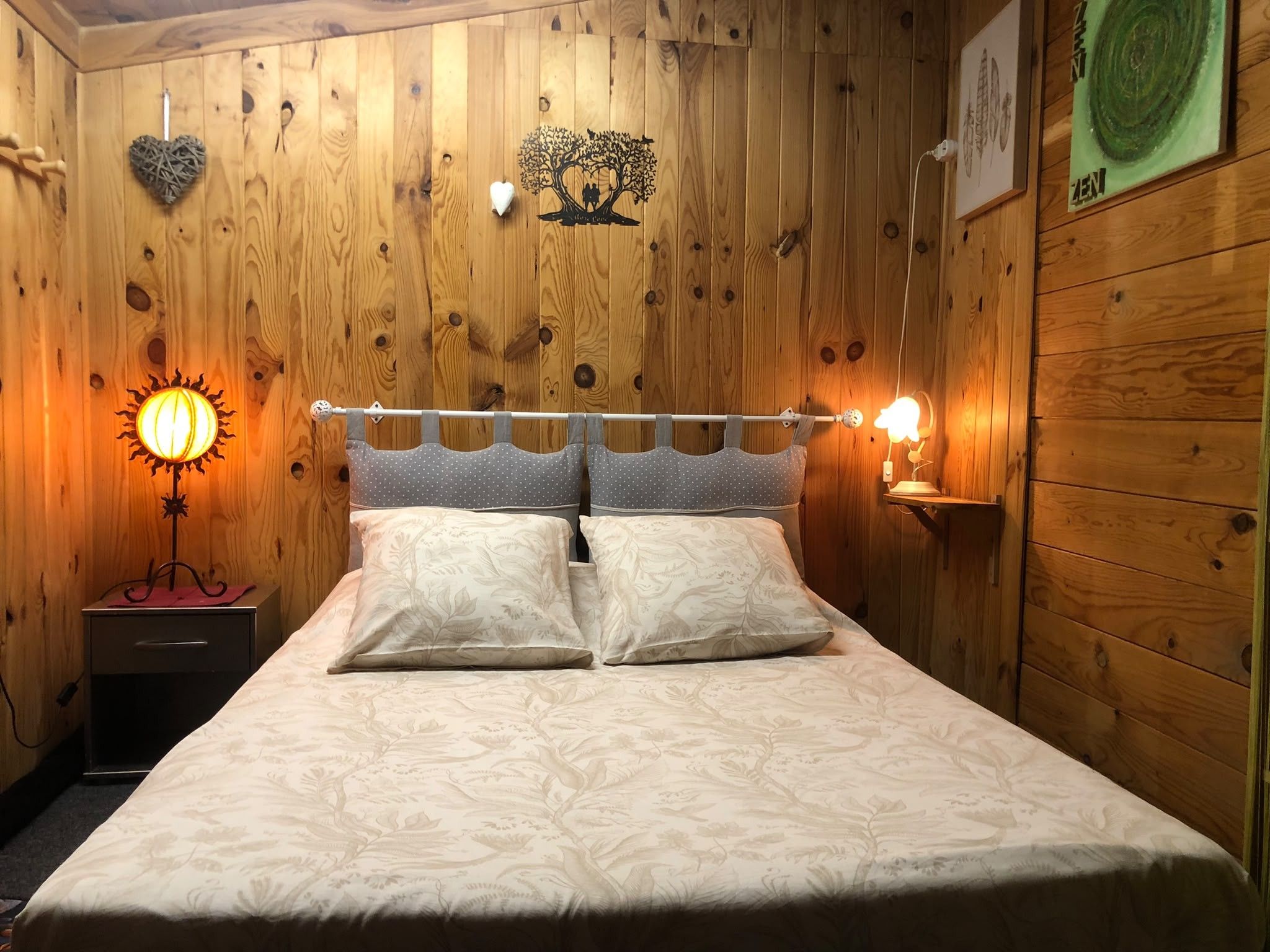 A wooden-paneled room with a bed, a nightstand, a wall-mounted lamp, and a wall decoration.