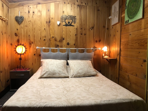 A wooden-paneled room with a bed, a nightstand, a wall-mounted lamp, and a wall decoration.