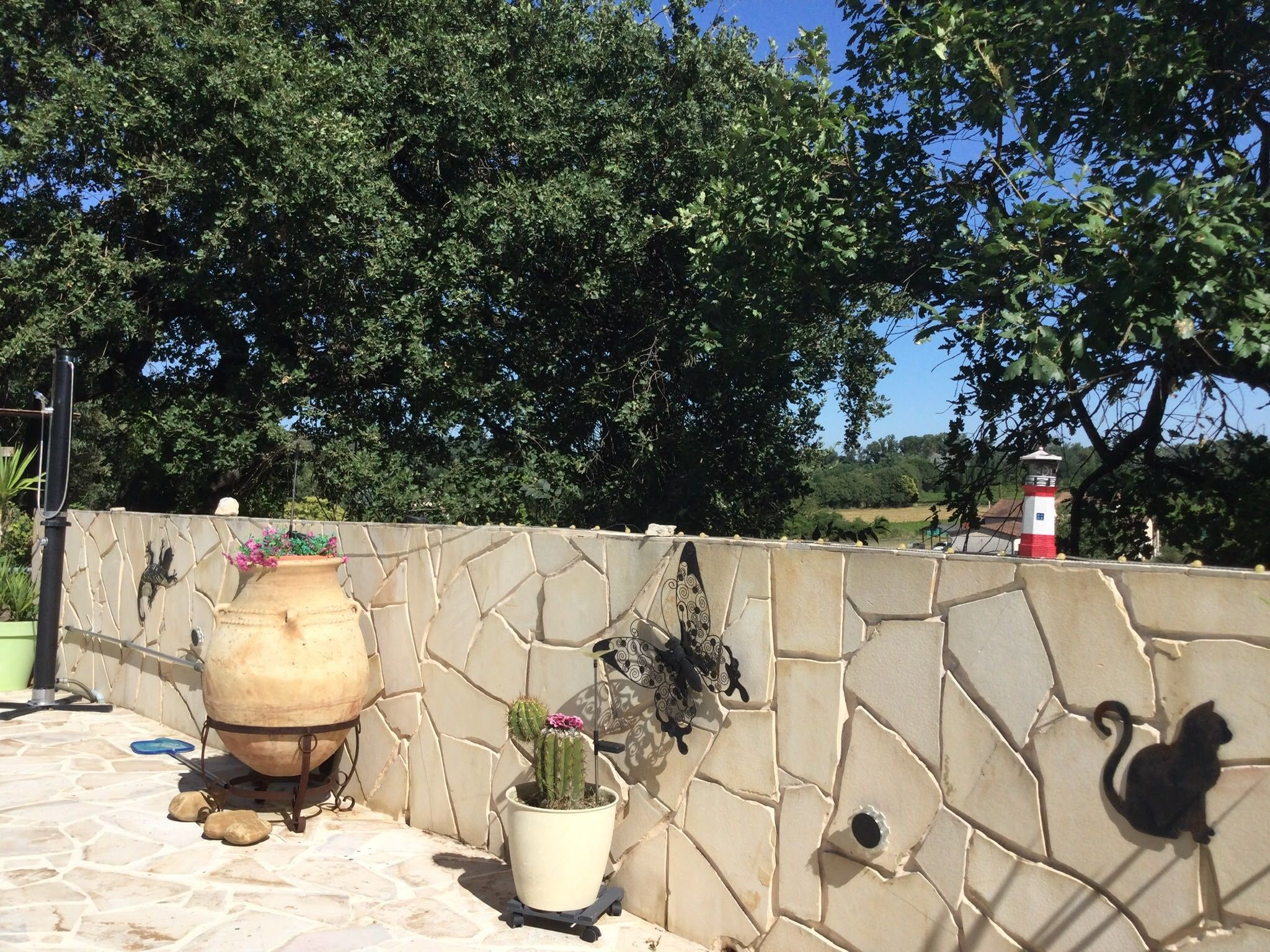 A stone wall with a butterfly sculpture, a large clay pot, and a potted plant.