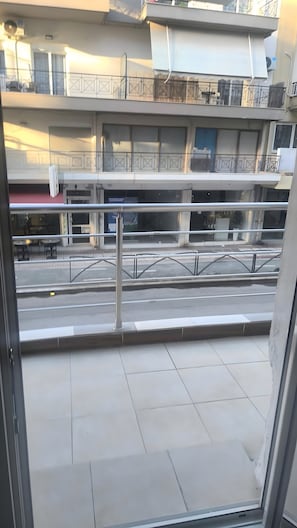 A view from a balcony with a metal railing, a tiled floor, and a street with parked cars.