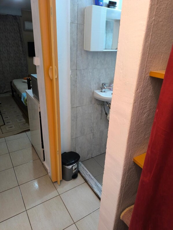 A narrow hallway with a tiled floor, a white sink, and a small trash bin. - Apartment 'Relax Place Alexandroupolis' with Balcony, Wi-Fi and Air Conditioning (Αλεξανδρούπολη)