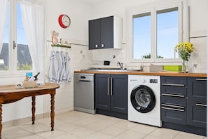 A modern kitchen with a dishwasher, washing machine, and a wooden table with kitchenware. - New Listing (Trégunc)