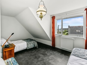 A bedroom with a sloped ceiling, a window with curtains, a radiator, and a bed with a patterned bedspread. - New Listing (Trégunc)