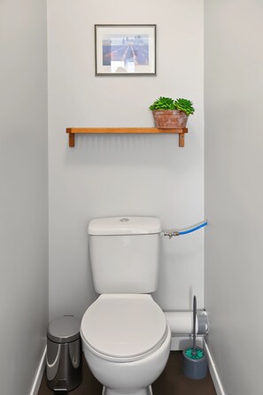 A small, modern bathroom with a toilet, bidet, trash bin, and a shelf with a potted plant. - New Listing (Trégunc)