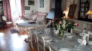 A dining area with a round table set for four, surrounded by white chairs, a vase with flowers, and a wall-mounted lamp.