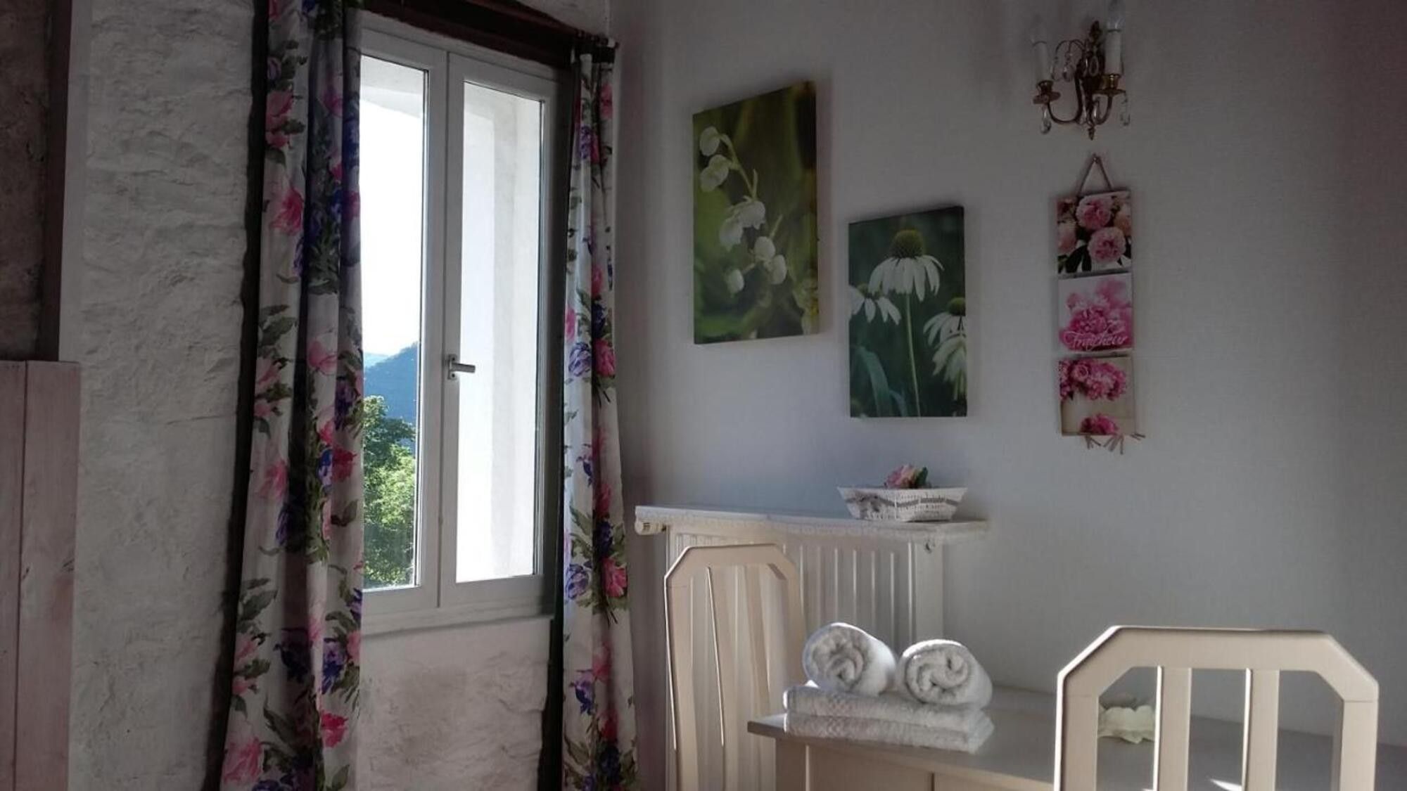 Une pièce avec une fenêtre, des rideaux à motifs floraux, un radiateur, un berceau et des tableaux accrochés au mur.