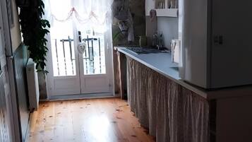 Une cuisine avec un plancher en bois, un réfrigérateur, un évier et une fenêtre avec un rideau.