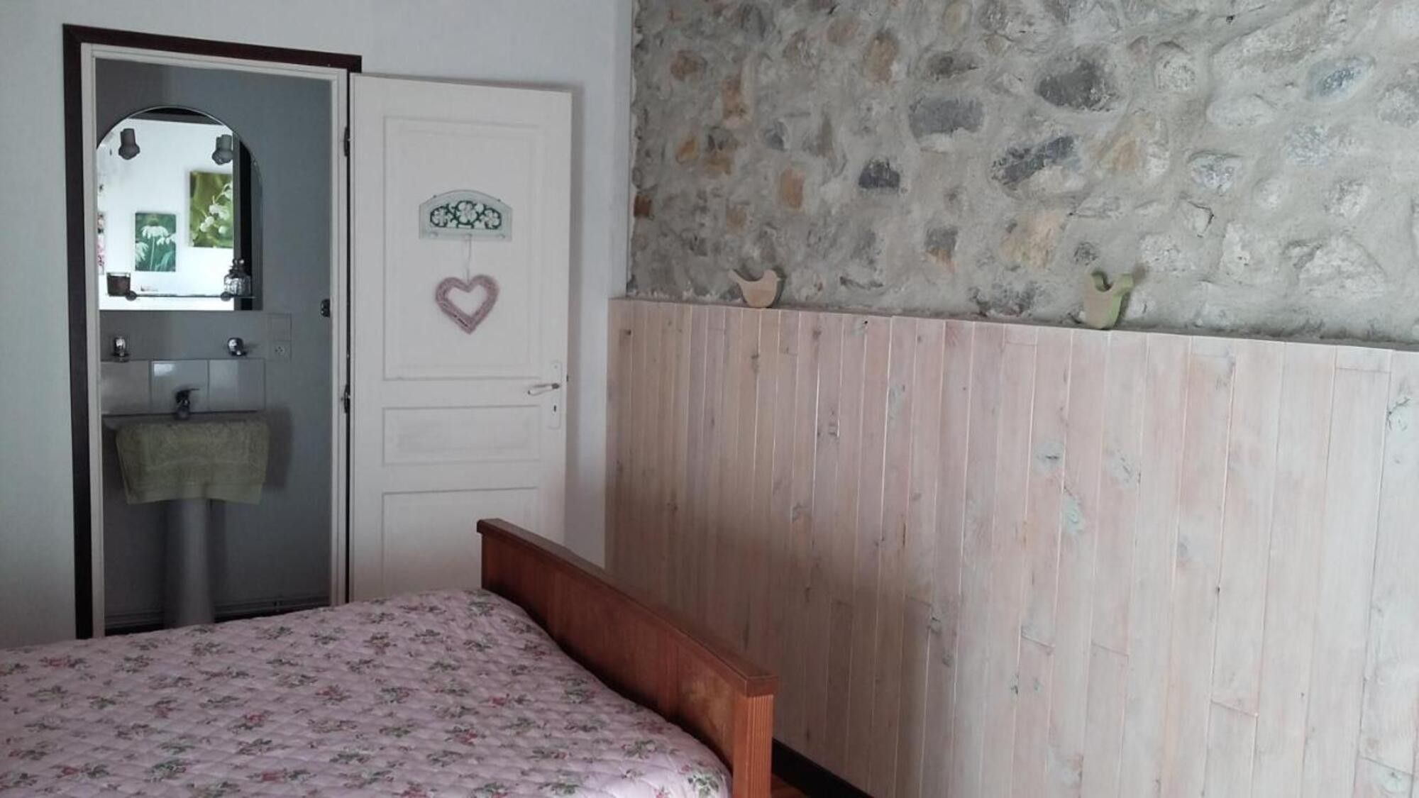 Een slaapkamer met een bed, een witte deur met een hartdecoratie, een stenen muur en een houten paneel.