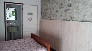 A bedroom with a bed, a white door with a heart decoration, a stone wall, and a wooden panel. - Bed and Breakfast 'Chambre Colibri' with Mountain View, Shared Terrace and Wi-Fi (Belvianes-et-Cavirac)