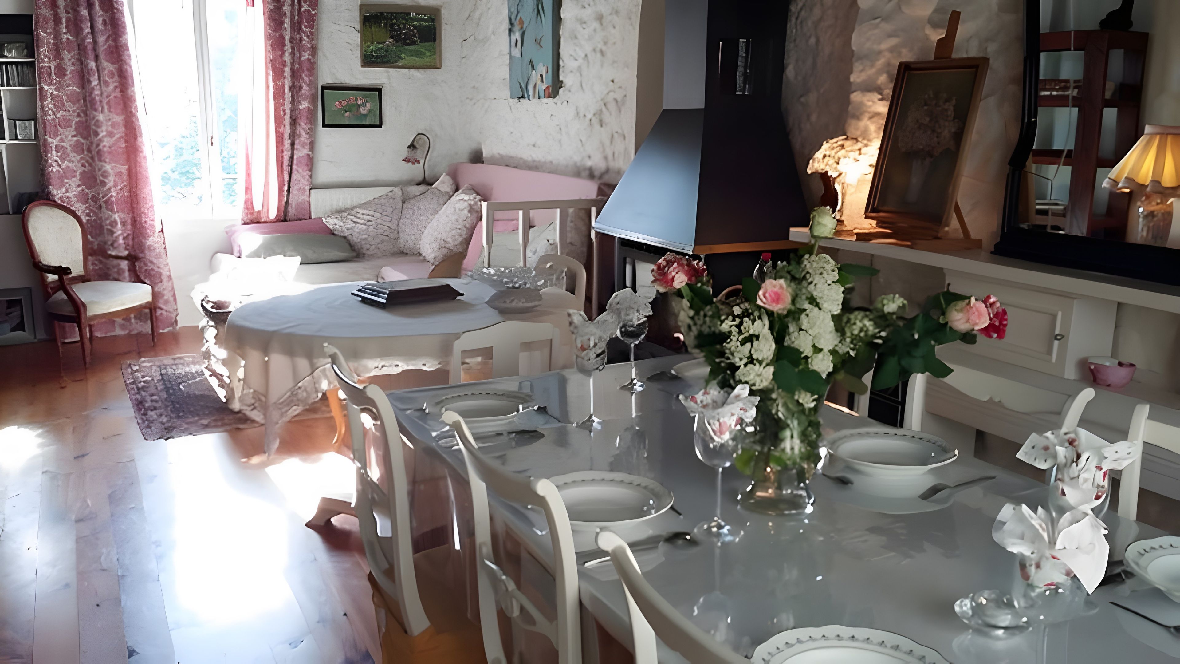 A dining area with a round table set for four, surrounded by white chairs, a vase with flowers, and a wall-mounted lamp.