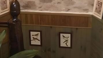 Een kamer met een stenen muur, een schilderij van een paard in een lijst, en twee afbeeldingen van vogels met een lijst.