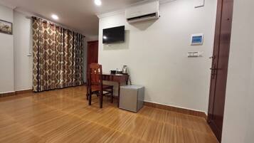 A room with a wooden floor, a TV mounted on the wall, a small refrigerator, and a door.