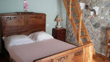 Un lit en bois avec une tête de lit, une table de chevet avec une lampe et un mur en pierre avec une échelle en bois.