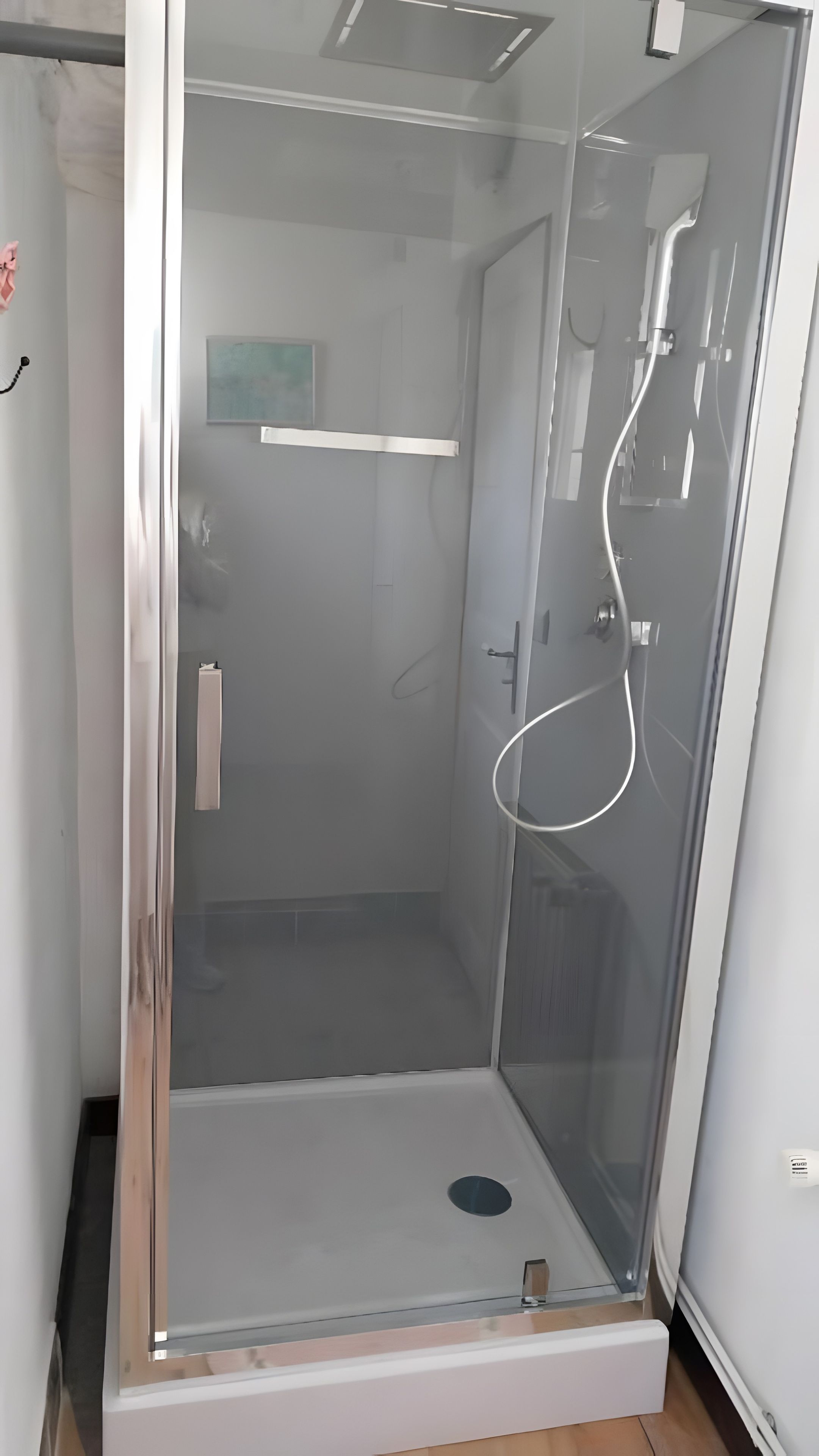 Une cabine de douche fermée par des parois en verre, dotée d’une porte, d’un porte-serviettes et d’un pommeau de douche.