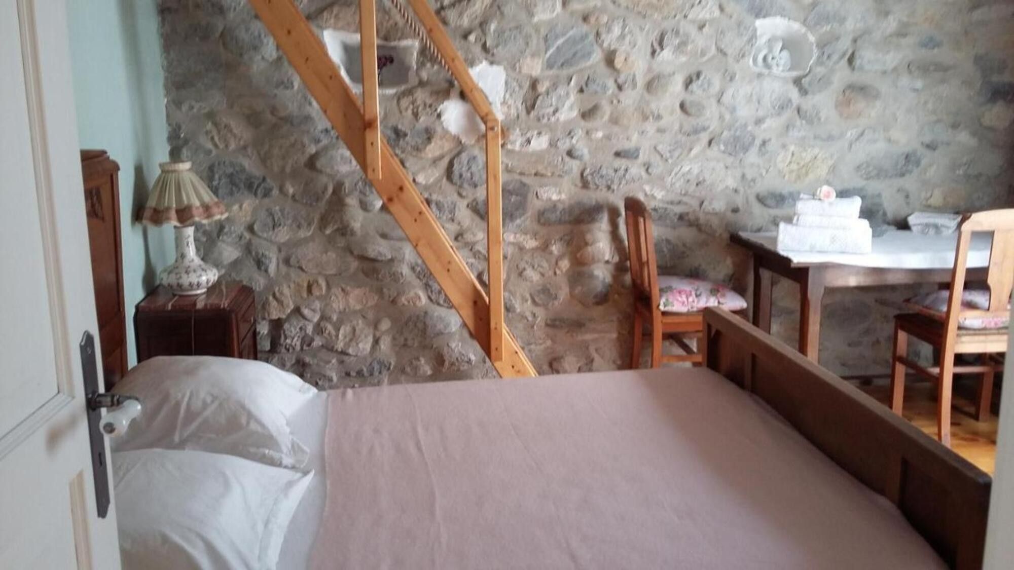 Une chambre avec un mur en pierre, un lit en bois, un bureau et une chaise.