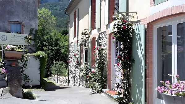 A narrow street with buildings on either side, some with flower boxes and greenery.