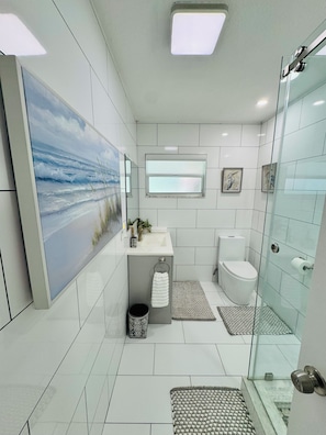 Uma casa de banho moderna com um quadro grande, uma janela, sanita e cabine de duche em vidro.