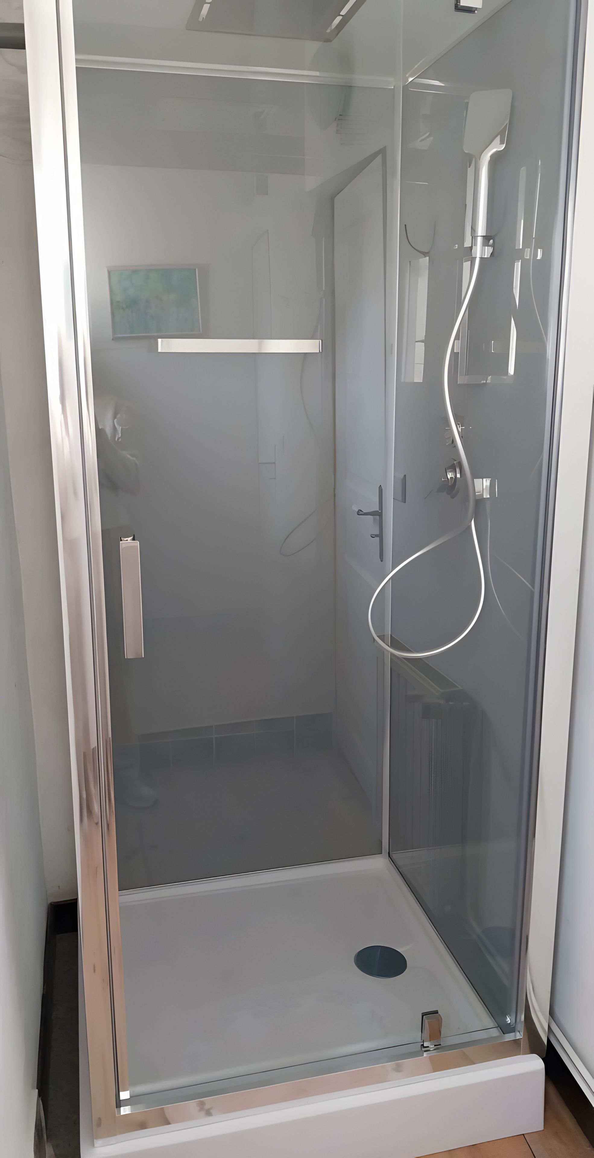 Cabina de ducha con vidrio, puerta, panel de control y desagüe visible.