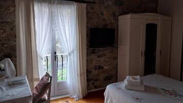 Une pièce avec un mur en pierre, un lit recouvert d’une couvre-lit à motifs floraux, une armoire et un téléviseur fixé au mur.