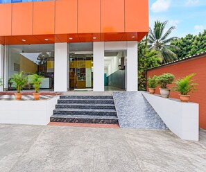 A modern building with a glass entrance, steps leading to the door, and potted plants on the ground. - Deluxe Hotel Sunshine (Gop)