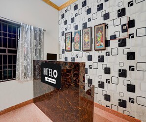 A hotel reception area with a marble counter, framed religious paintings on the wall, and a sign indicating it is serviced by OYO. - Deluxe Hotel Sunshine (Gop)